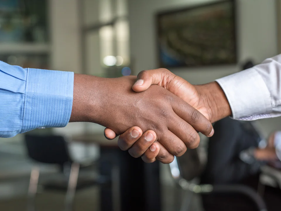 Two people shaking hands across a table in an office