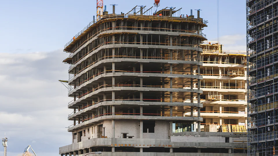 A concrete frame going up, floor by floor, on a city plot